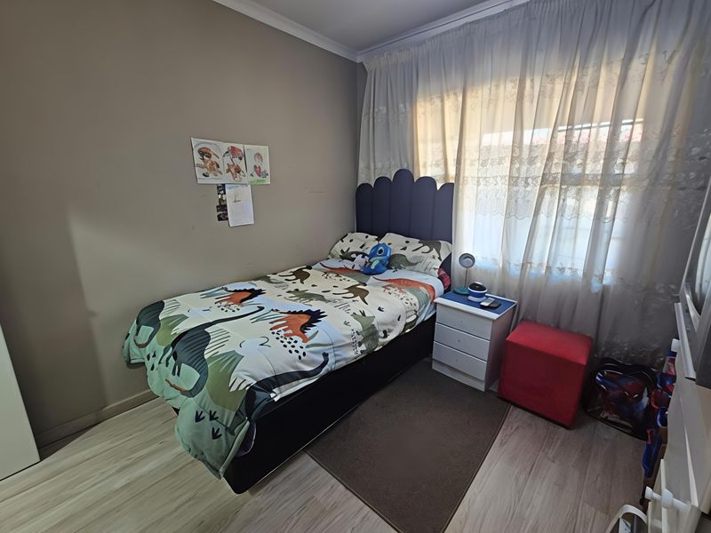 A functional bedroom featuring light-toned laminate flooring and large windows with curtain treatments, providing a neutral base for personalization.