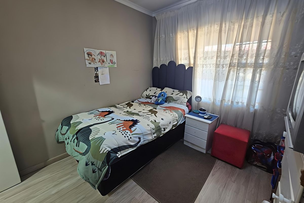 A functional bedroom featuring light-toned laminate flooring and large windows with curtain treatments, providing a neutral base for personalization.