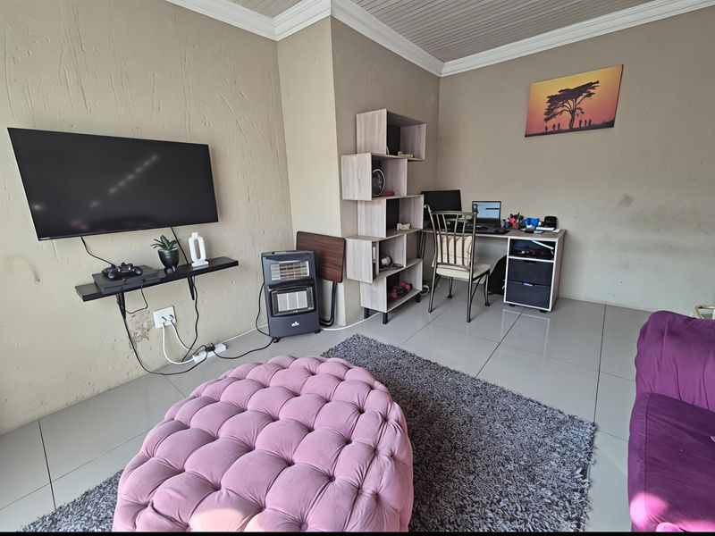 A living room area featuring tiled flooring and crown molding, currently utilized as a combined lounge and home office space.