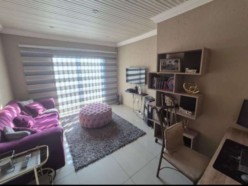 A cozy living room featuring tiled flooring, a tongue and groove ceiling with recessed lighting, and a sliding door with modern roller blinds.
