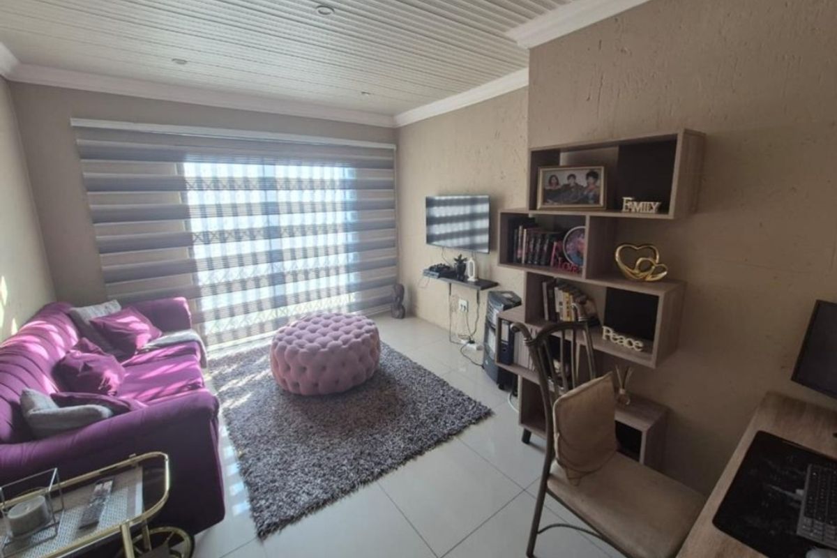 A cozy living room featuring tiled flooring, a tongue and groove ceiling with recessed lighting, and a sliding door with modern roller blinds.