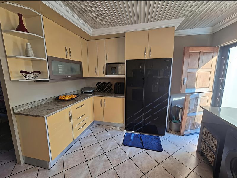 A functional kitchen featuring light-toned cabinetry, stone-look countertops, tiled flooring, and a distinctive panelled ceiling with a stable door leading outdoors.