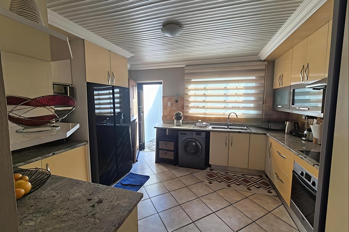 A functional kitchen featuring built-in cabinetry, stone countertops, integrated oven and hob, tiled flooring, and a slatted ceiling with direct access to an outdoor area.