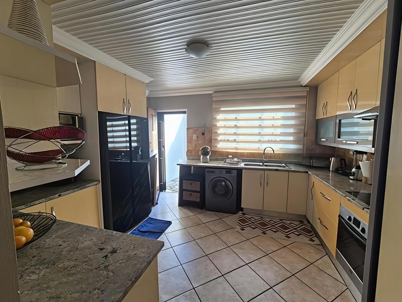 A functional kitchen featuring built-in cabinetry, stone countertops, integrated oven and hob, tiled flooring, and a slatted ceiling with direct access to an outdoor area.