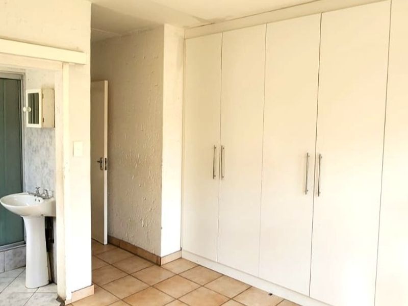 A spacious bedroom featuring extensive built-in cupboards and an en-suite bathroom with a pedestal basin and shower enclosure.
