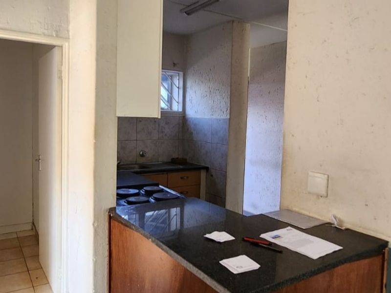A dated kitchen area featuring a breakfast bar, built-in cabinetry, and a hob, offering significant potential for modernization and renovation.