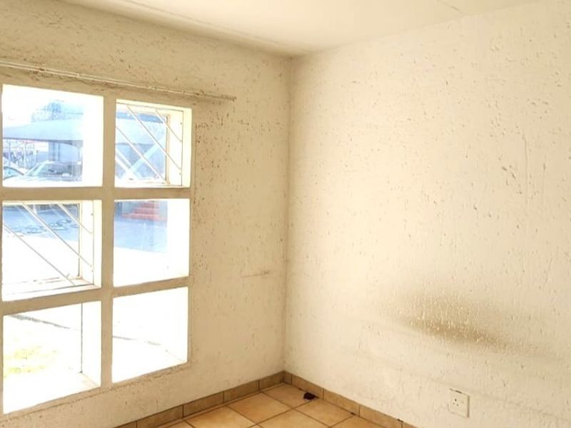An empty living room featuring tiled flooring and large grid-pattern windows with security bars, requiring significant wall repairs and cosmetic updates.