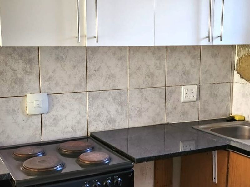 A functional kitchen area featuring granite countertops, a built-in electric stove, and a double sink, currently requiring minor repairs to the backsplash and cabinetry.