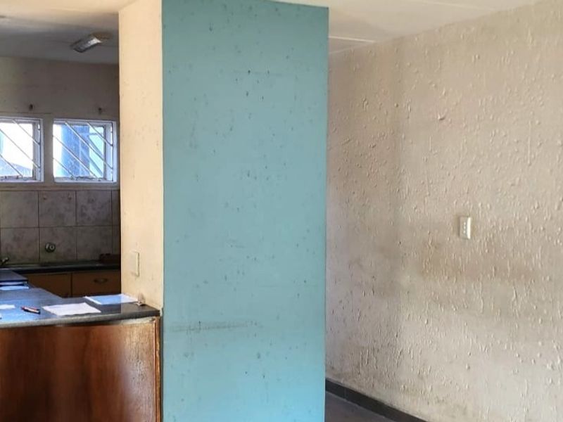 An open-plan living and kitchen area featuring dated cabinetry, a tiled backsplash, and textured walls, offering a blank canvas for renovation.