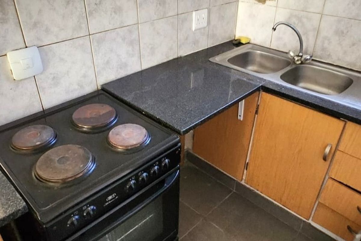 A functional kitchen area featuring granite countertops, a double bowl sink, and a built-in electric stove with tiled backsplash.