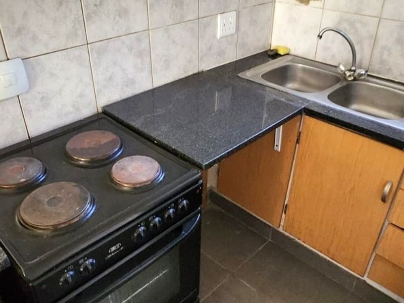 A functional kitchen area featuring granite countertops, a double bowl sink, and a built-in electric stove with tiled backsplash.