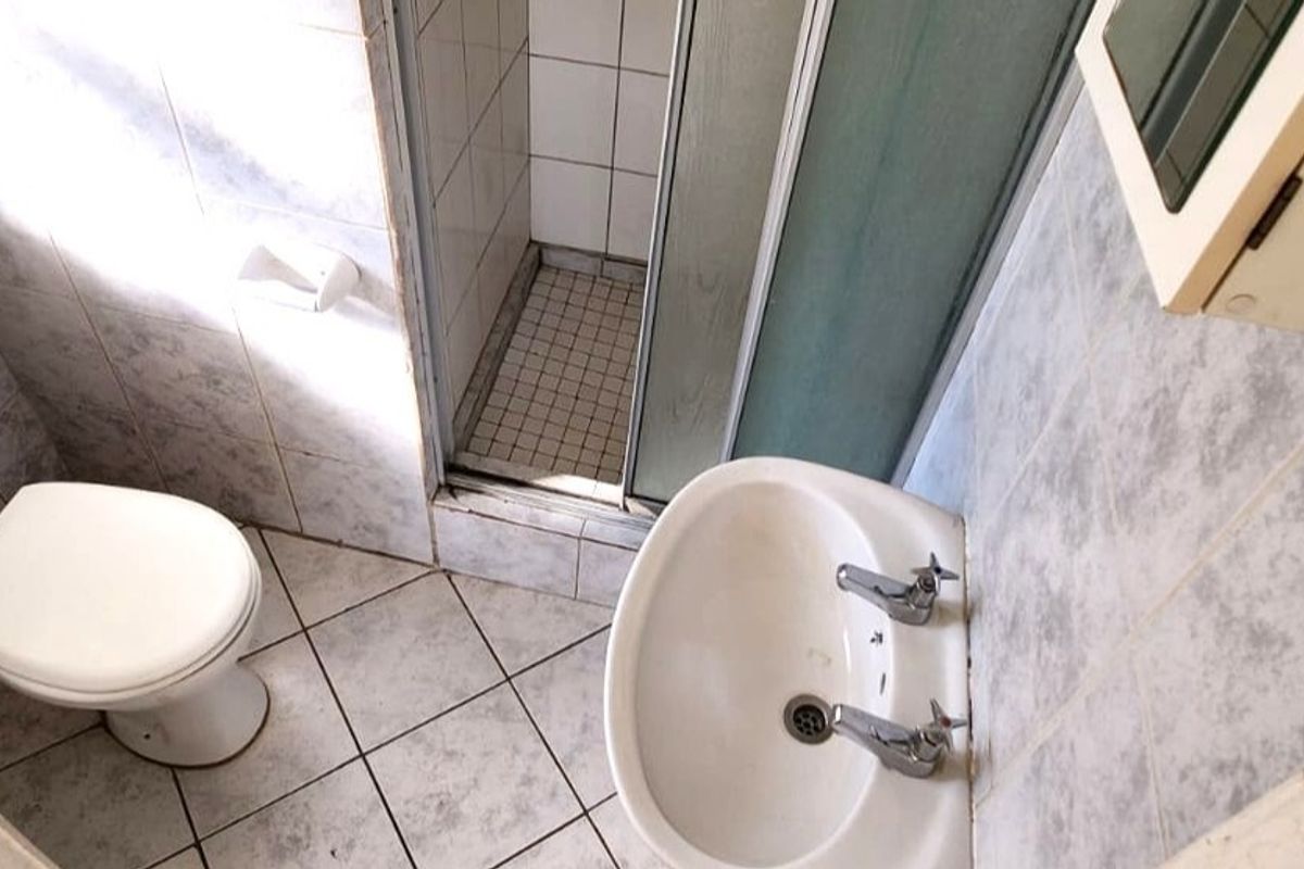 A compact bathroom featuring a shower enclosure, pedestal basin, and toilet with dated tiled finishes throughout.