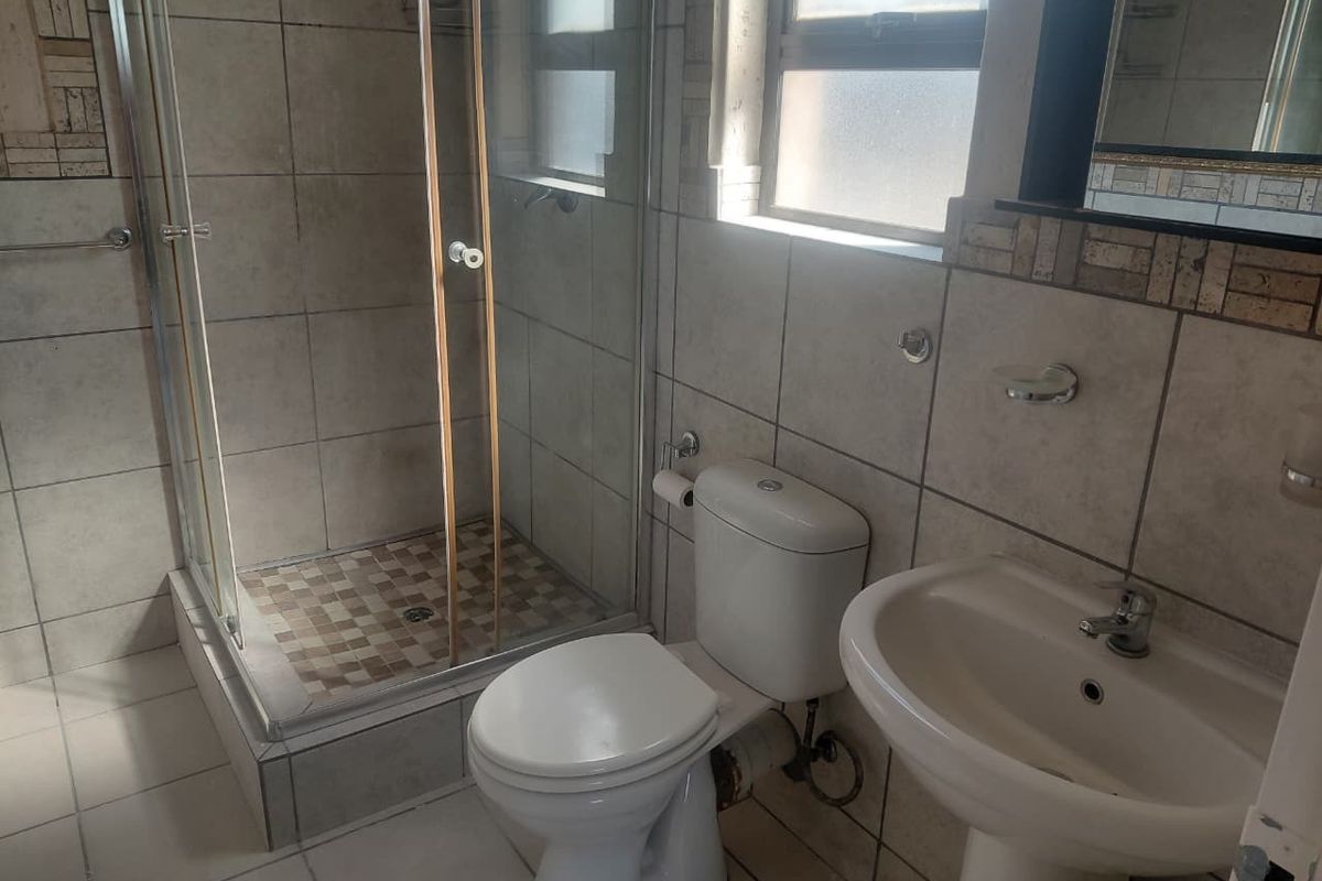 A functional bathroom featuring a shower enclosure, pedestal basin, and toilet with neutral wall and floor tiling.