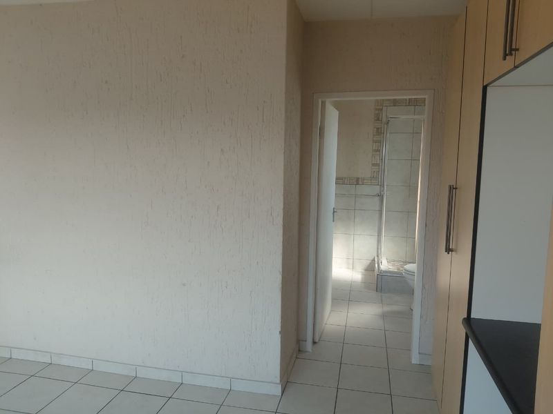 A clean, empty hallway featuring tiled flooring, textured walls, and built-in storage cupboards, providing direct access to an adjacent bathroom.