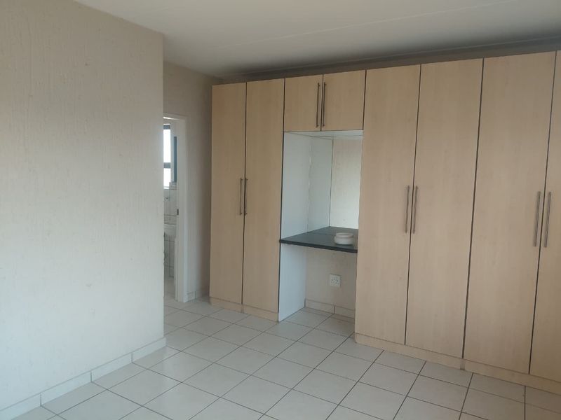 A spacious bedroom featuring neutral tiled flooring and extensive built-in cupboards with an integrated vanity area, offering ample storage and a clean, functional layout.