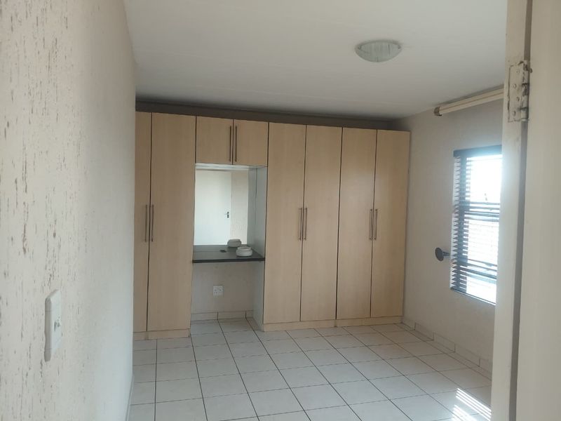 A vacant bedroom featuring built-in cupboards with an integrated vanity area, tiled flooring, and venetian blinds.