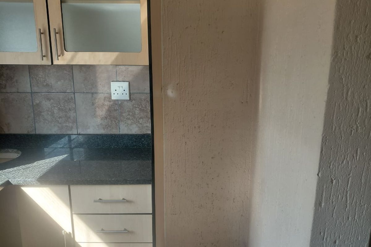 A compact kitchen area featuring granite countertops, built-in cabinetry, and a tiled backsplash, requiring minor cosmetic attention to the wall surfaces.