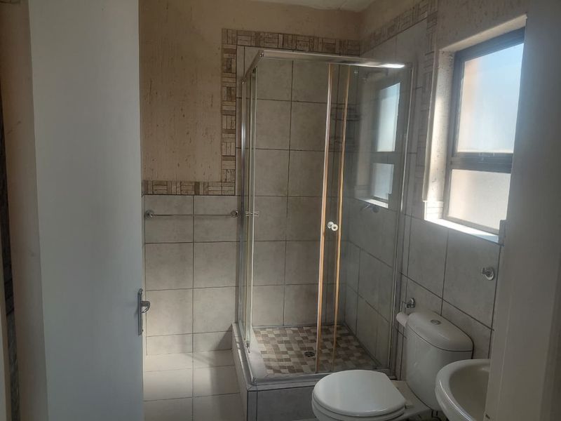 A functional bathroom featuring a glass shower enclosure, tiled walls, a standard toilet, and a pedestal basin with natural light from the window.