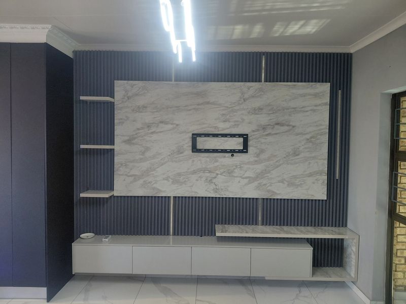 A modern living room featuring a custom built-in media unit with slatted wall paneling, marble-effect accents, and sleek floating shelving.
