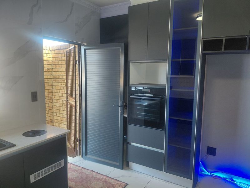Modern kitchen featuring dark cabinetry, built-in oven, quartz countertops, and marble-effect wall tiles, with direct access to an exterior courtyard.