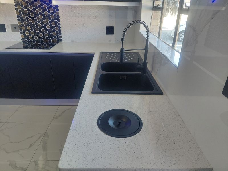 Modern kitchen featuring quartz countertops, a double basin sink with a gooseneck faucet, built-in induction hob, and stylish hexagonal mosaic tile backsplash.