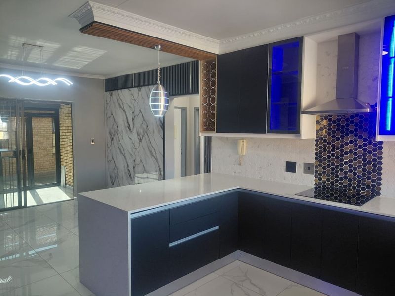 Modern kitchen featuring sleek dark cabinetry, stone countertops, a honeycomb tile backsplash, integrated extractor fan, and stylish feature wall cladding.