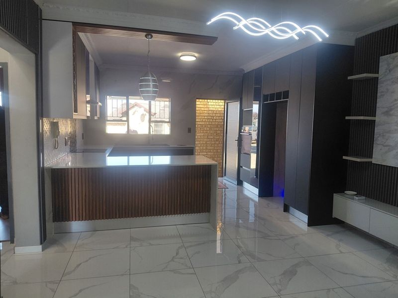 Modern open-plan living and kitchen area featuring high-end finishes, marble-look floor tiles, custom slatted wood cabinetry, and contemporary lighting fixtures.