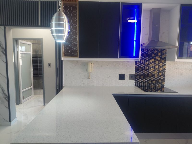Modern kitchen featuring quartz countertops, dark cabinetry, a stylish hexagon tile backsplash, and integrated appliances, offering a clean and contemporary culinary space.