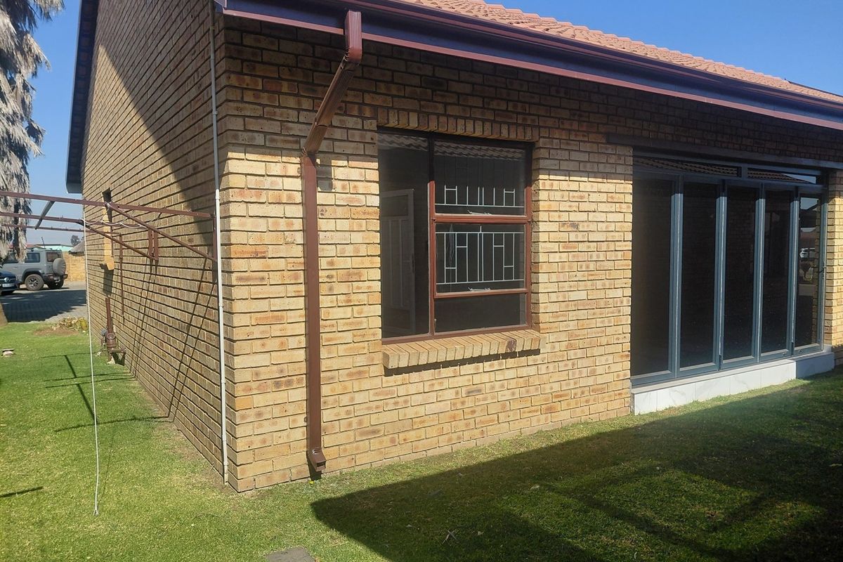 Rear view of the townhouse featuring face brick exterior, tiled roof, aluminium window frames with security bars, and sliding glass doors leading to the garden.