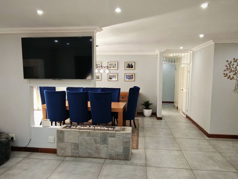 Spacious open-plan living and dining area featuring tiled flooring, recessed lighting, and a central stone-clad fireplace partition.