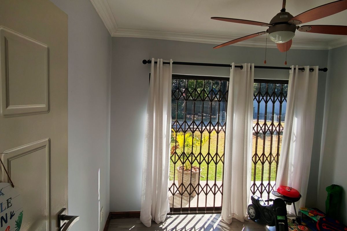 A bedroom featuring laminate flooring, a ceiling fan, and a sliding door with a security gate providing access to the garden.