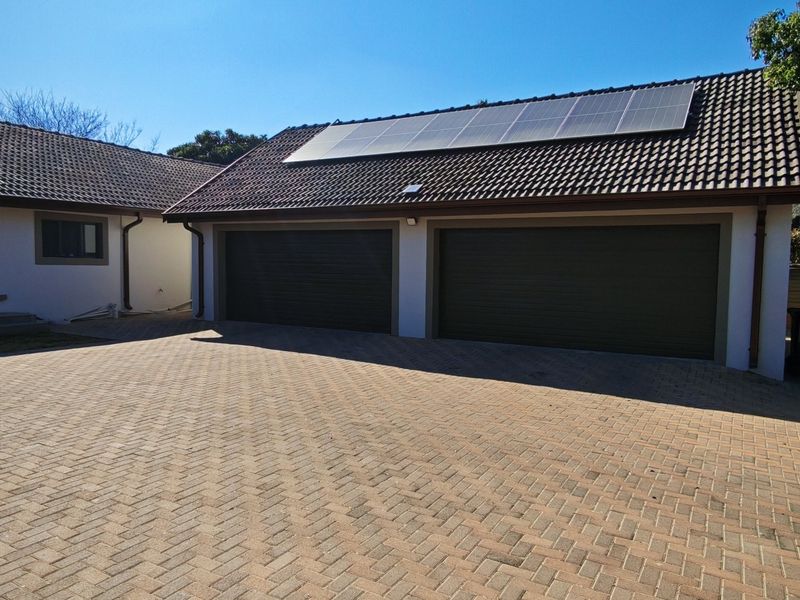 Front view of the property featuring a spacious paved driveway, a double garage with automated doors, and roof-mounted solar panels.