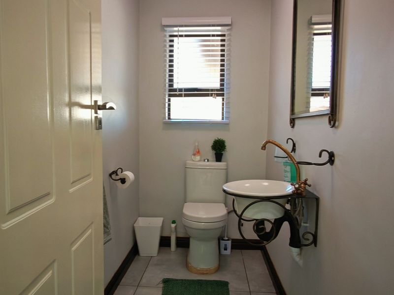 A compact guest bathroom featuring a wall-mounted basin, toilet, tiled flooring, and a window with venetian blinds.