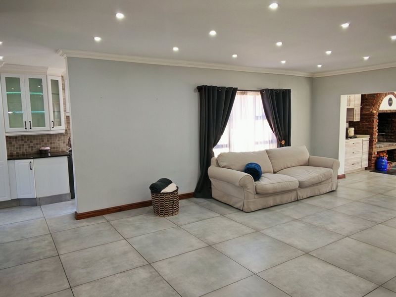 Spacious open-plan living area featuring large format floor tiles, recessed lighting, a stone-clad fireplace, and a seamless transition into the adjacent kitchen space.