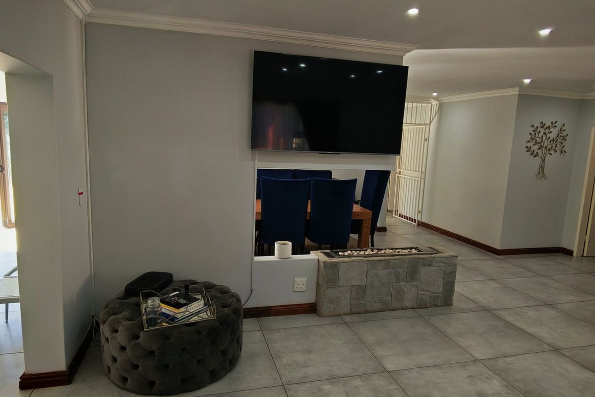 Spacious living area featuring tiled flooring, recessed lighting, and a central stone-clad fireplace, with direct access to an outdoor patio space.