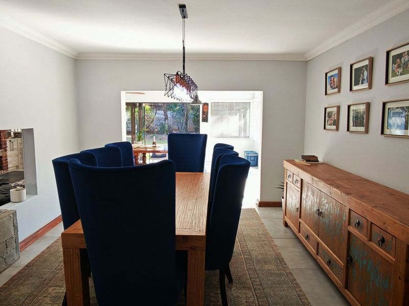 Spacious dining room featuring tiled flooring, cove cornicing, and a built-in stone-clad fireplace, with an open-plan flow to the kitchen and outdoor area.