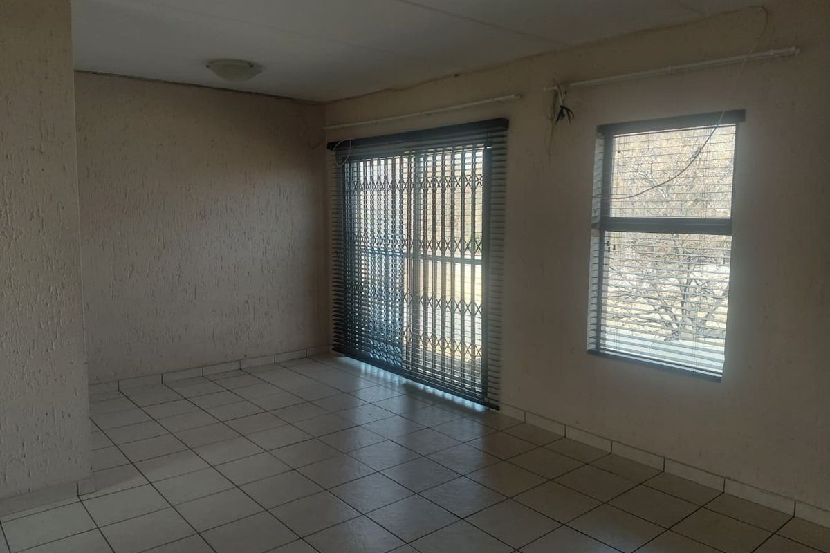 An empty living room featuring tiled flooring, a sliding glass door with security gate, and window blinds. The space requires minor cosmetic updates.