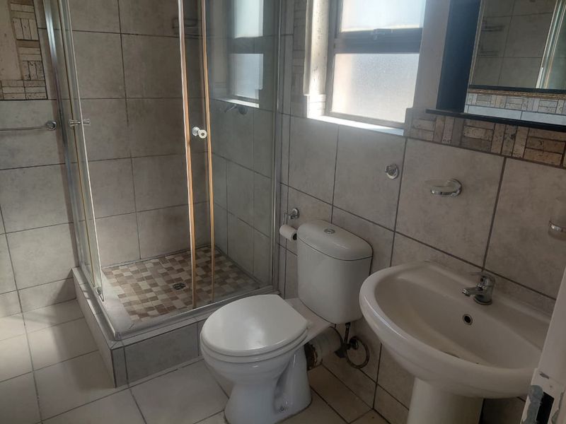 A functional bathroom featuring a glass shower enclosure, pedestal basin, and toilet with neutral wall and floor tiling.