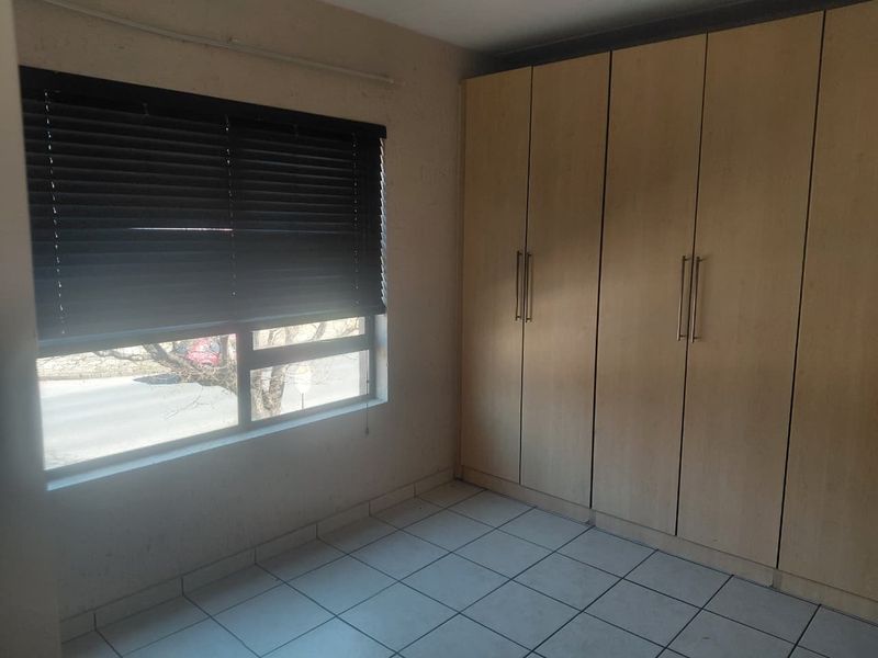 A functional bedroom featuring tiled flooring, built-in wooden cupboards, and a window fitted with venetian blinds.