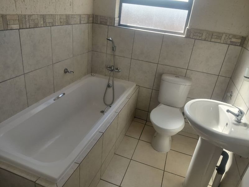A functional bathroom featuring a bathtub, pedestal basin, and toilet with neutral tiled finishes and a frosted window for natural light.