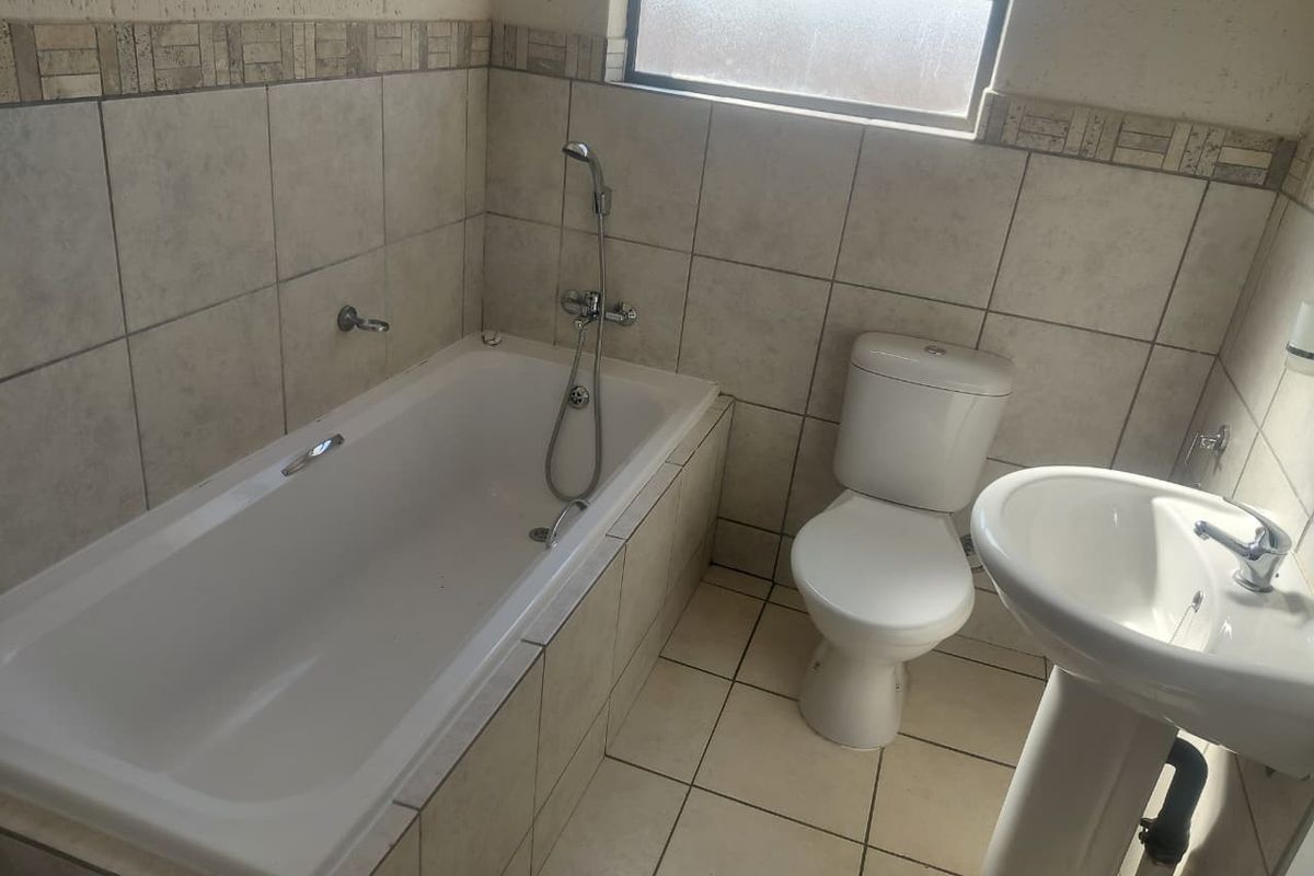 A functional bathroom featuring a bathtub, pedestal basin, and toilet with neutral tiled finishes and a frosted window for natural light.