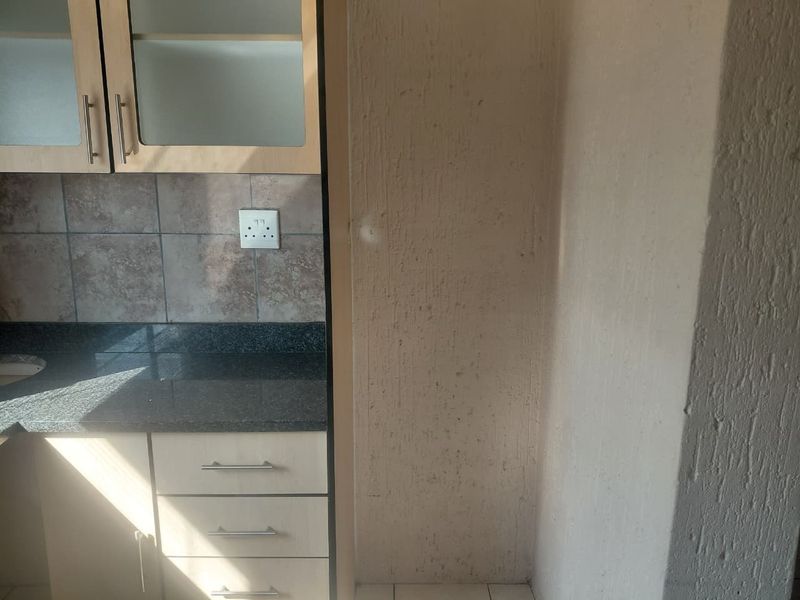 A compact kitchen area featuring built-in cabinetry, granite countertops, and a tiled backsplash, requiring minor cosmetic updates to the wall finishes.