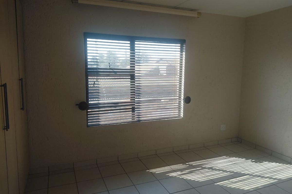 An empty bedroom featuring tiled flooring, built-in cupboards, and venetian blinds, offering a neutral canvas for personalization.