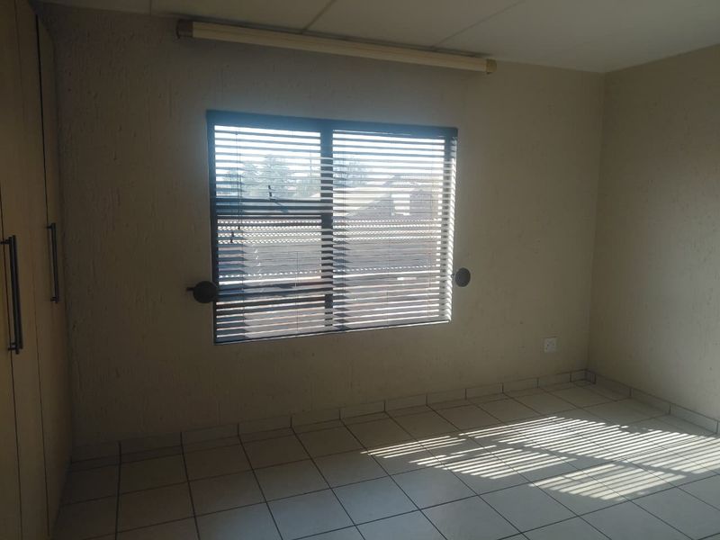 An empty bedroom featuring tiled flooring, built-in cupboards, and venetian blinds, offering a neutral canvas for personalization.