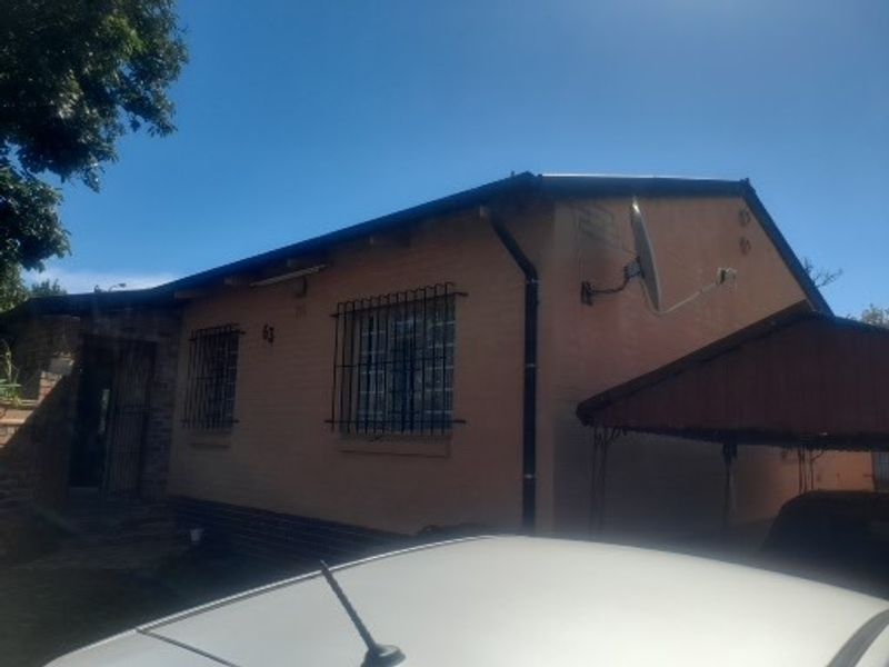 Front elevation of a single-story house featuring a carport, security bars on windows, and a satellite dish installation.