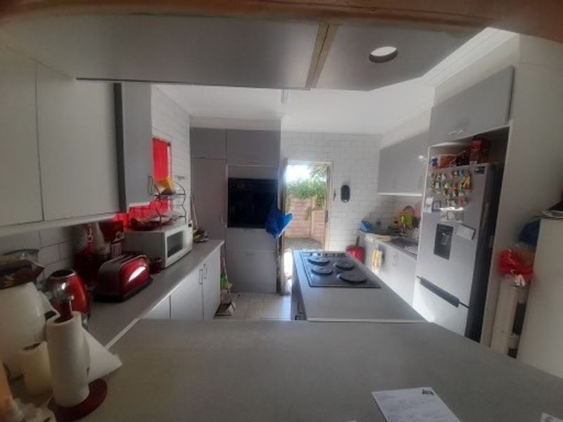 A functional kitchen featuring built-in cabinetry, a central island with an integrated electric hob, and a built-in oven, with direct access to the rear exterior.
