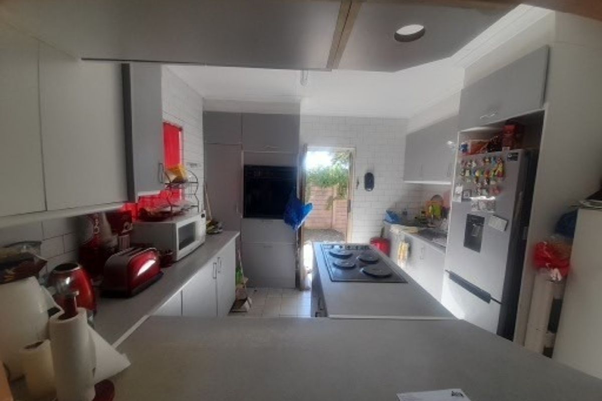A functional kitchen featuring built-in cabinetry, a central island with an integrated electric hob, and a built-in oven, with direct access to the rear exterior.