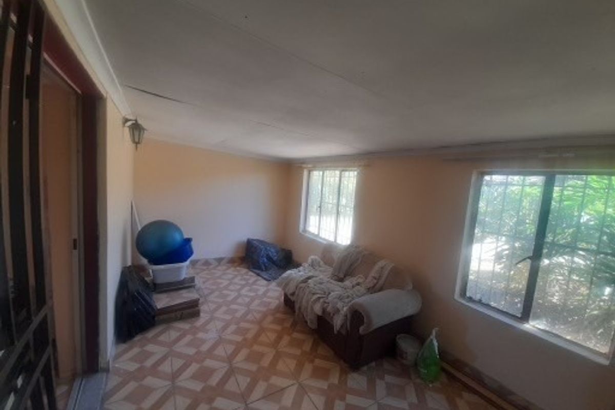 A living area featuring tiled flooring, security bars on the windows, and a wall-mounted light fixture, showing signs of wear on the ceiling.