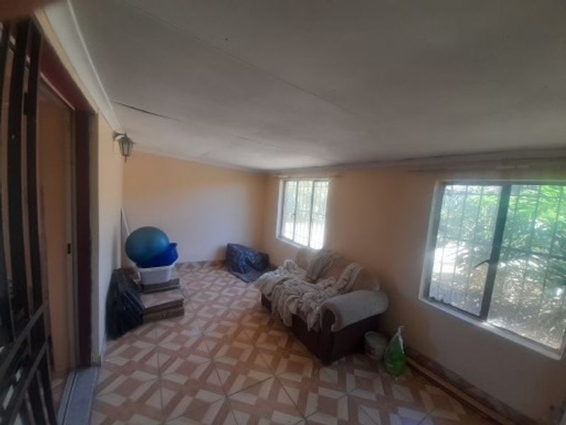 A living area featuring tiled flooring, security bars on the windows, and a wall-mounted light fixture, showing signs of wear on the ceiling.