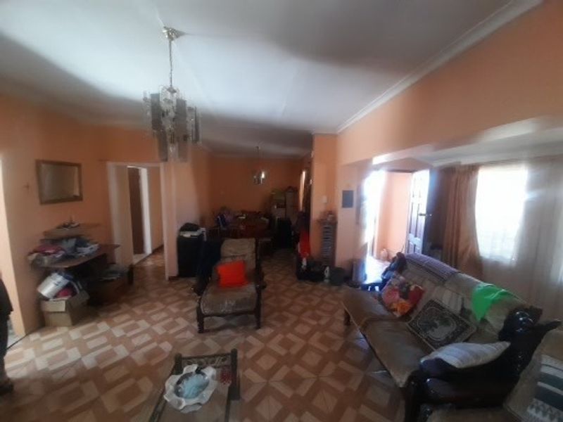 A living room area featuring tiled flooring, ceiling cornicing, and a central pendant light fixture, currently showing signs of wear and dated finishes.